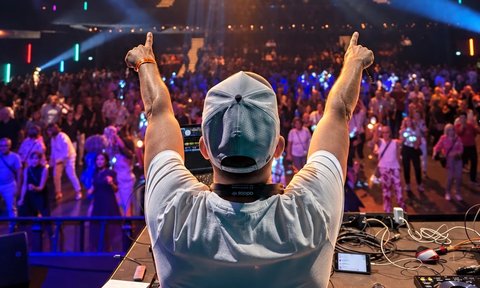 Nik Thomi von hinten am DJ-Pult mit erhobenen Daumen vor tanzendem Publikum und Discokugel