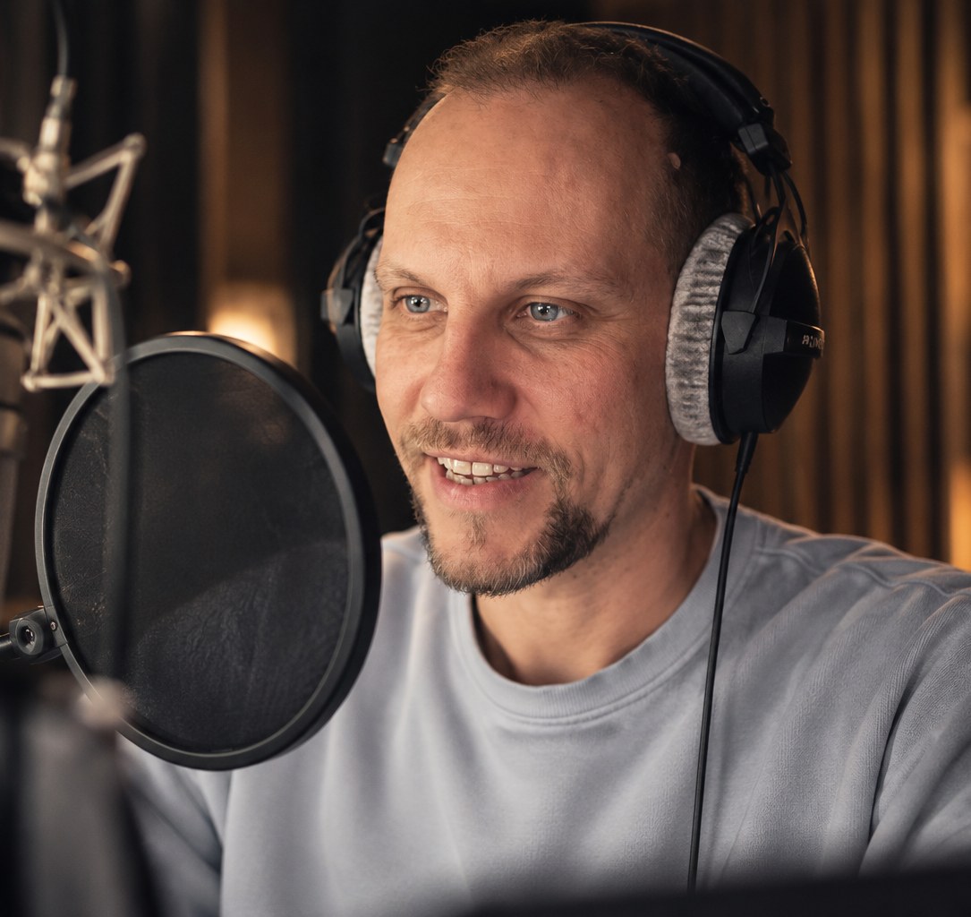 Nik Thomi mit Kopfhörern vor seinem Neumann TLM 103 in seinem Aufnahmestudio